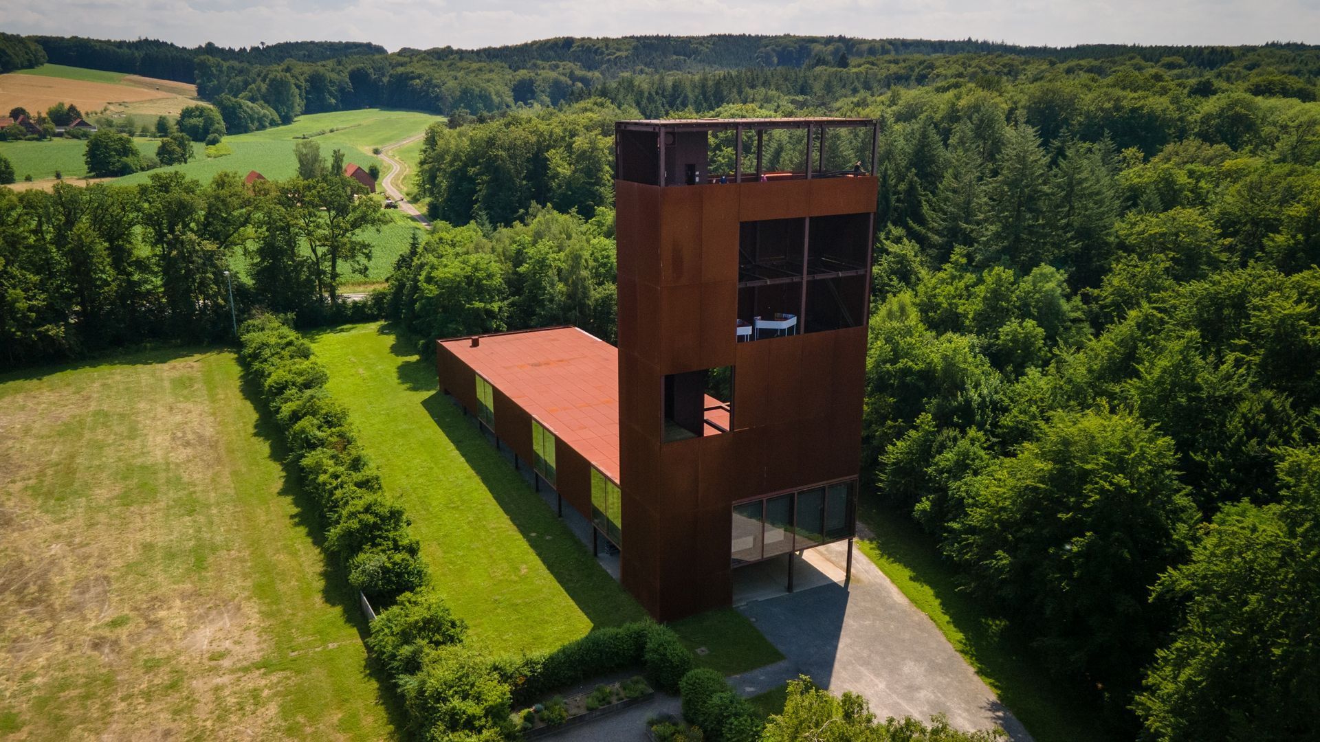 Panoramablick auf den Museumsturm des Museum und Park Kalkriese in dem sich Tagungsräume befinden. Der Turm liegt im Museumspark, umgeben von Wald und grünen Wiesen.
